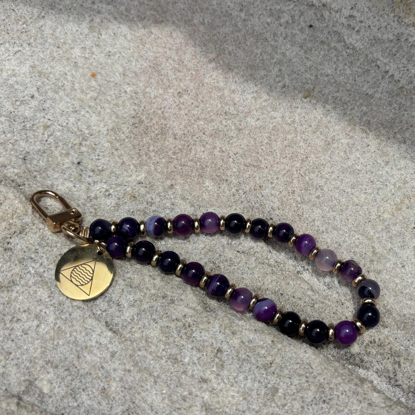 Beaded phone chain with a gold tag on a textured stone surface