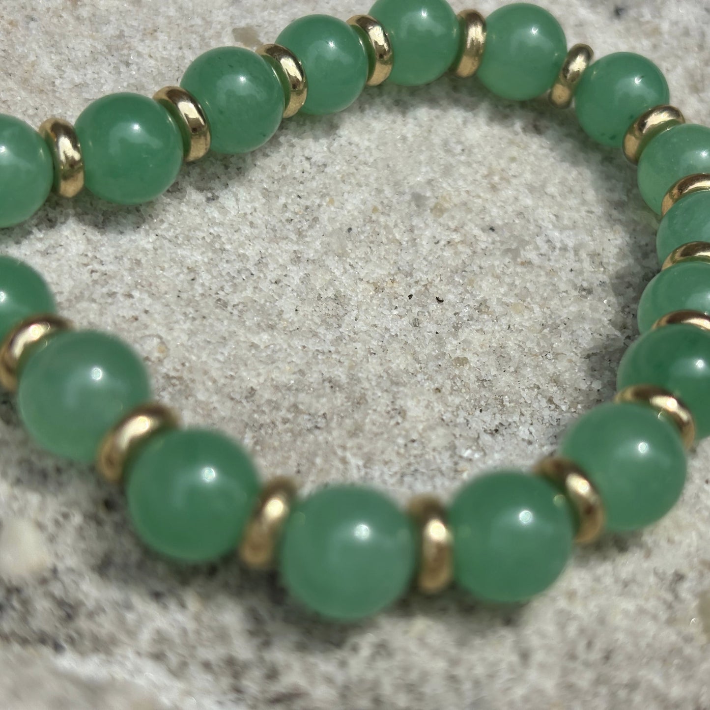 Green beaded bracelet with gold accents on a textured surface