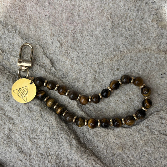 Beaded keychain with a gold tag on a stone surface
