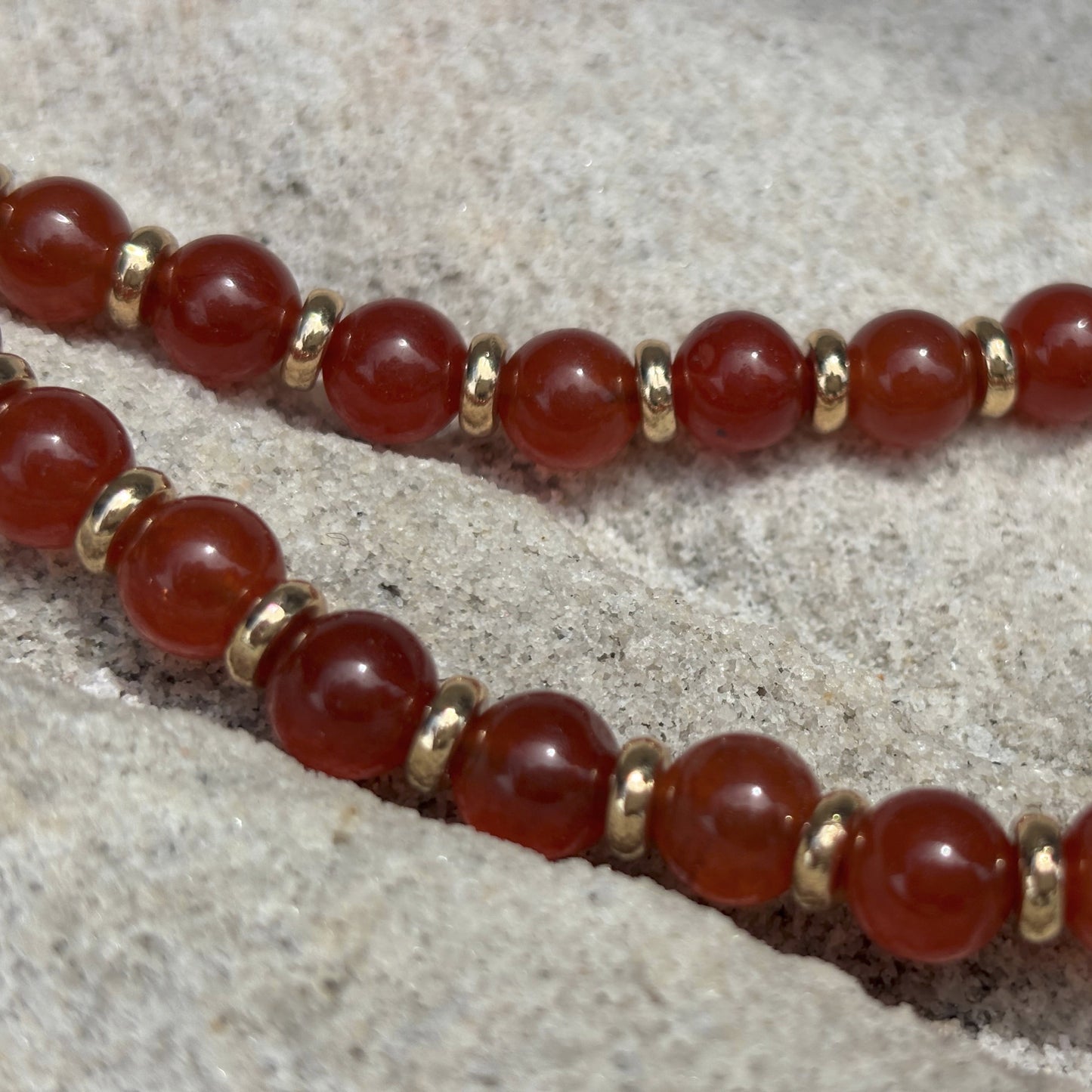 Bracelet with red beads and gold accents on a stone surface