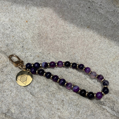 Beaded phone chain with a gold tag on a textured stone surface