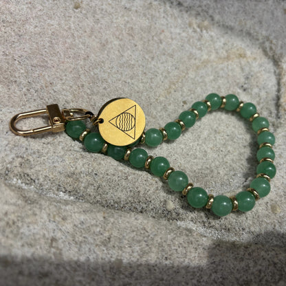 Green beaded phone chain with gold clasp on a textured surface