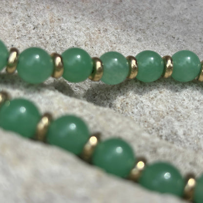 Green beaded bracelet with gold accents on a textured surface