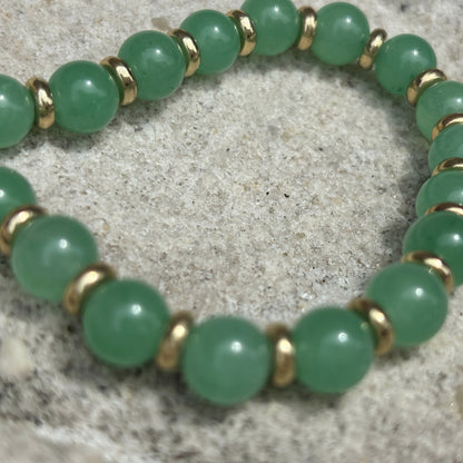 Green beaded bracelet with gold accents on a textured surface