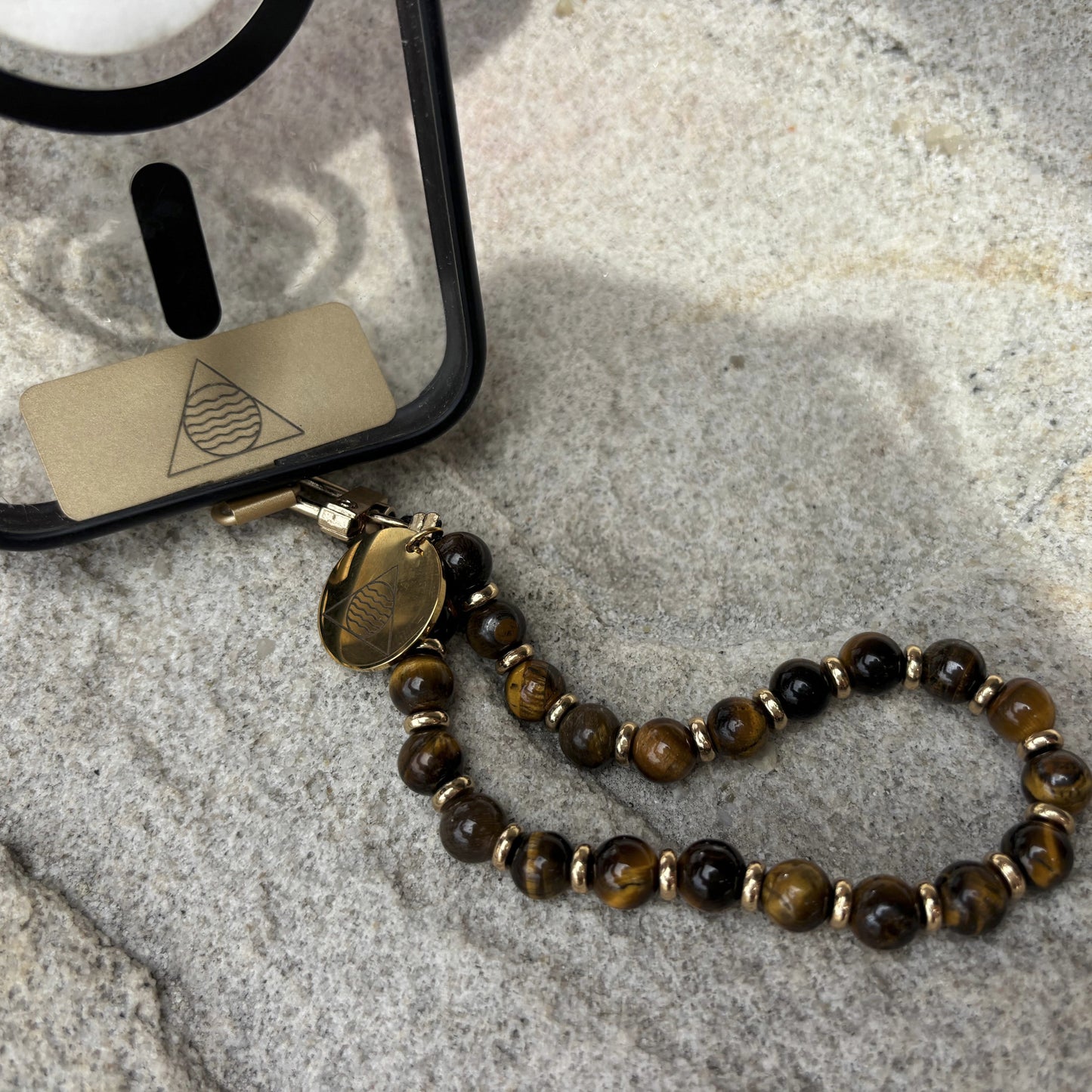 Phone case with a beaded lanyard on a textured stone surface