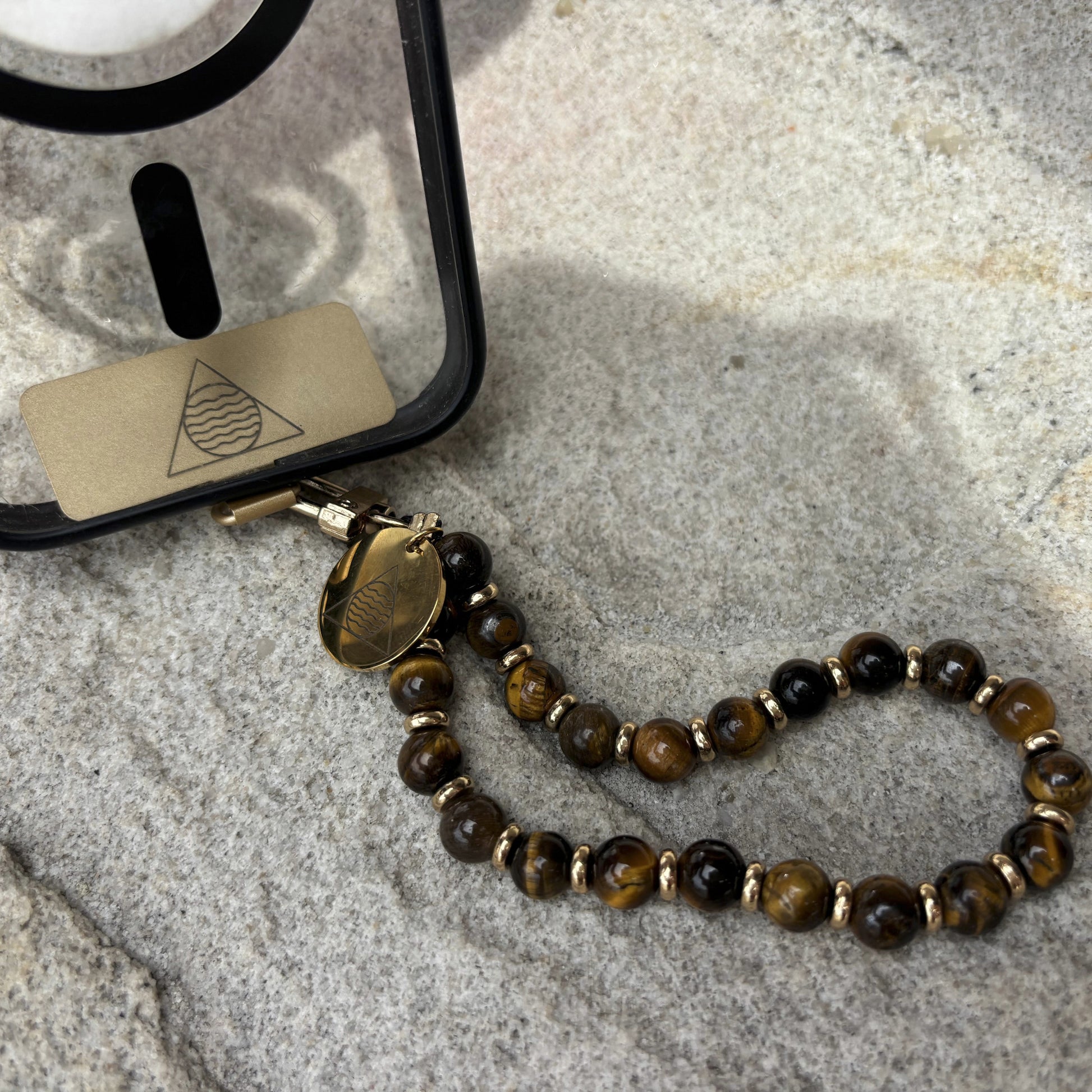 Phone case with a beaded lanyard on a textured stone surface