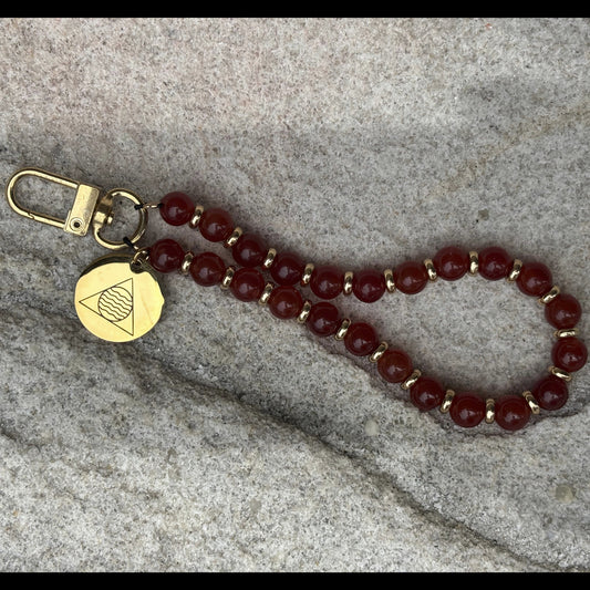 Beaded keychain with gold clasp and tag on a stone surface