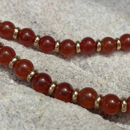 Bracelet with red beads and gold accents on a stone surface