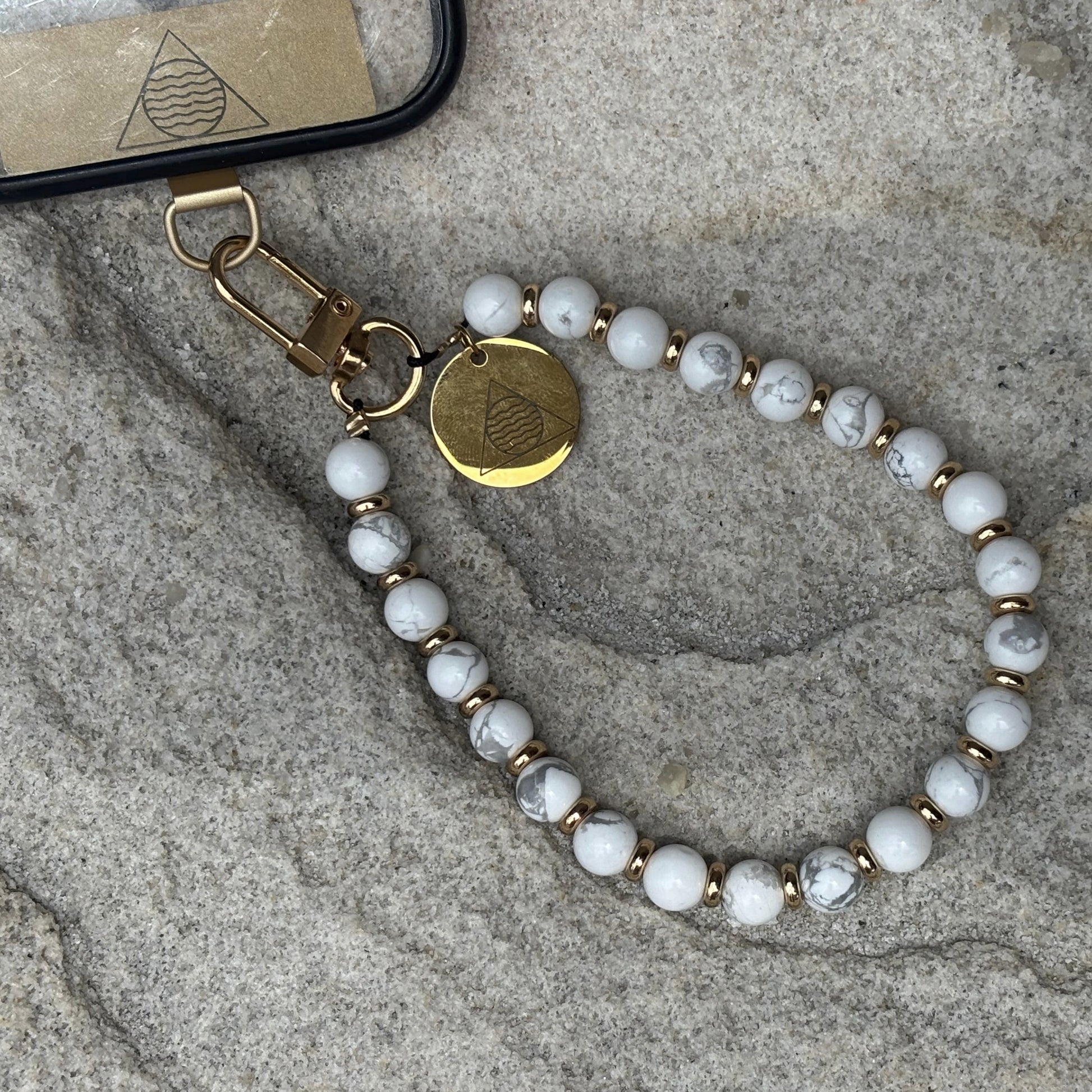 Beaded phone chain with gold accents on a textured surface