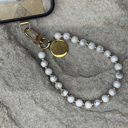 Beaded phone chain with gold accents on a textured surface