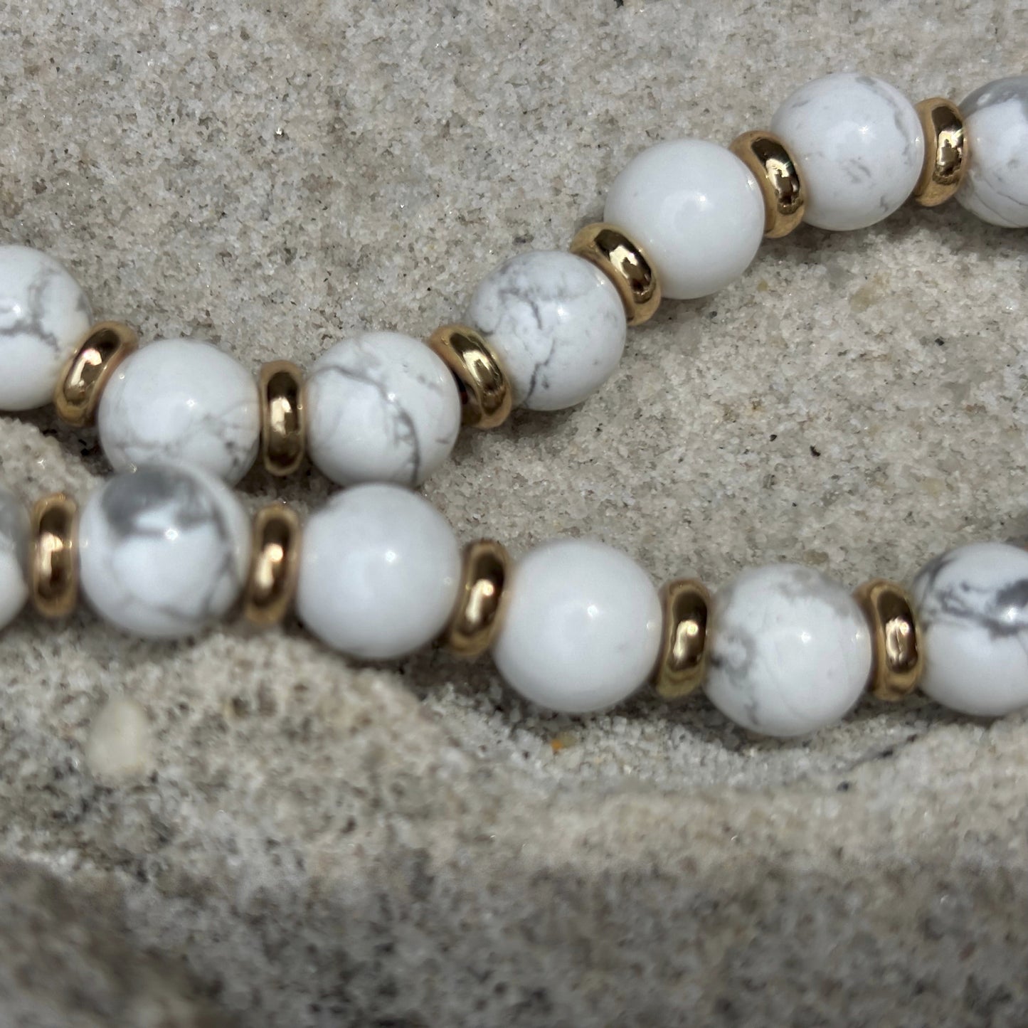 Phone chain with white beads and gold accents on a textured surface