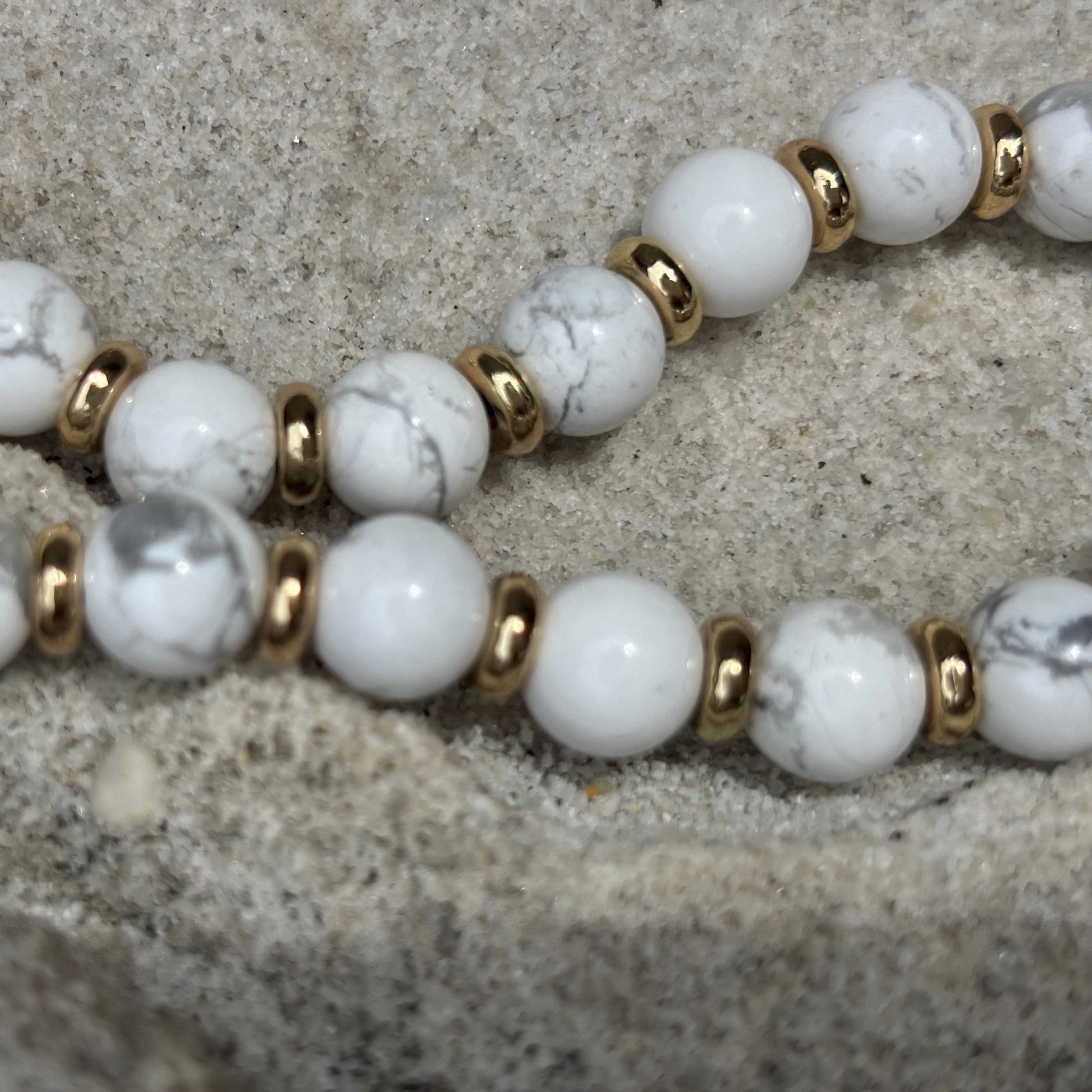 Phone chain with white beads and gold accents on a textured surface