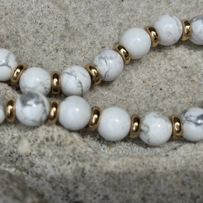 Phone chain with white beads and gold accents on a textured surface