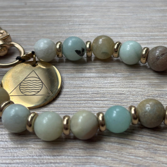 Phone bracelet with green beads and gold accents on a wooden surface